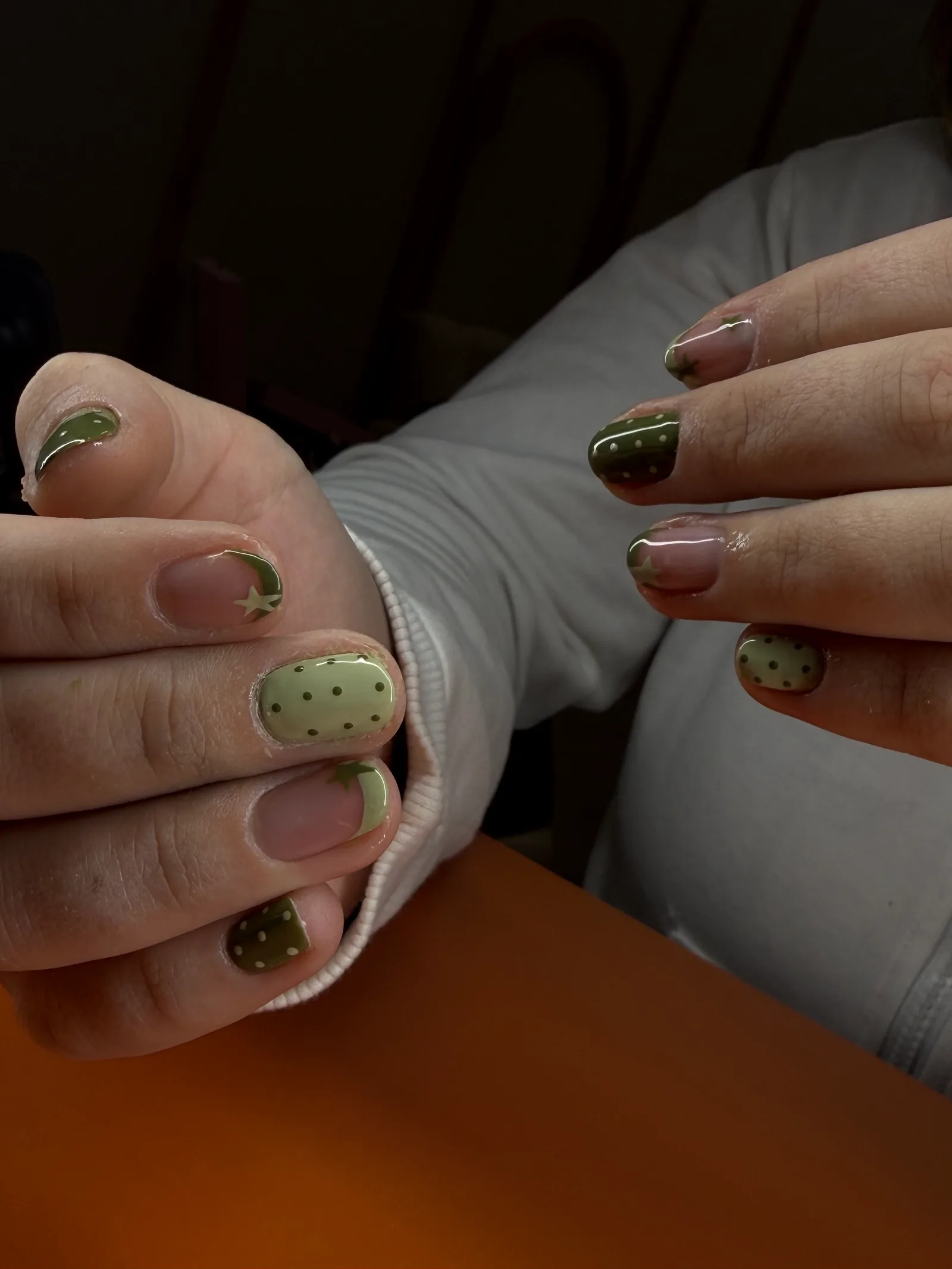 Unhas curtas decoradas em tons de verde, com estrelas, luas e bolinhas